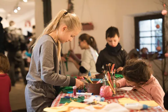 Children doing Christmas crafts at a table with colored paper, pencils, and decorations